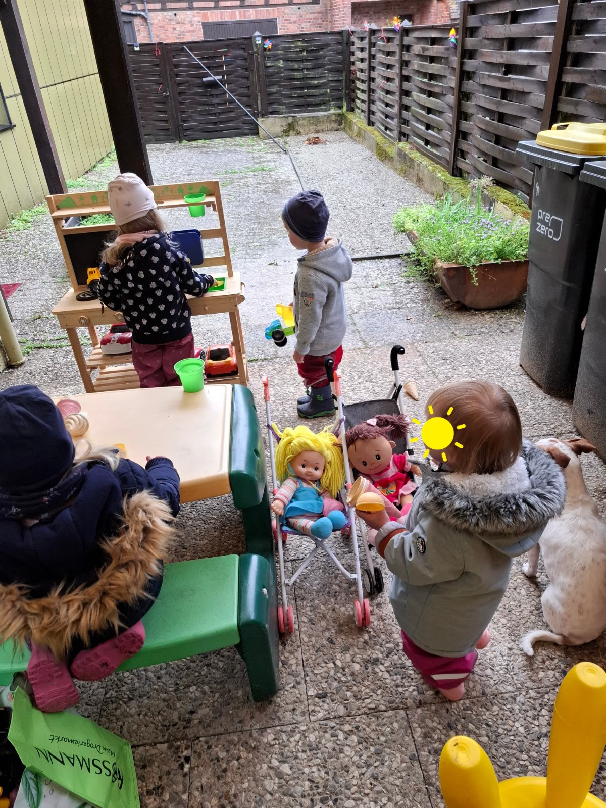 Kinder spielen draußen mit Spielküche, Puppenwagen und Fahrzeugen