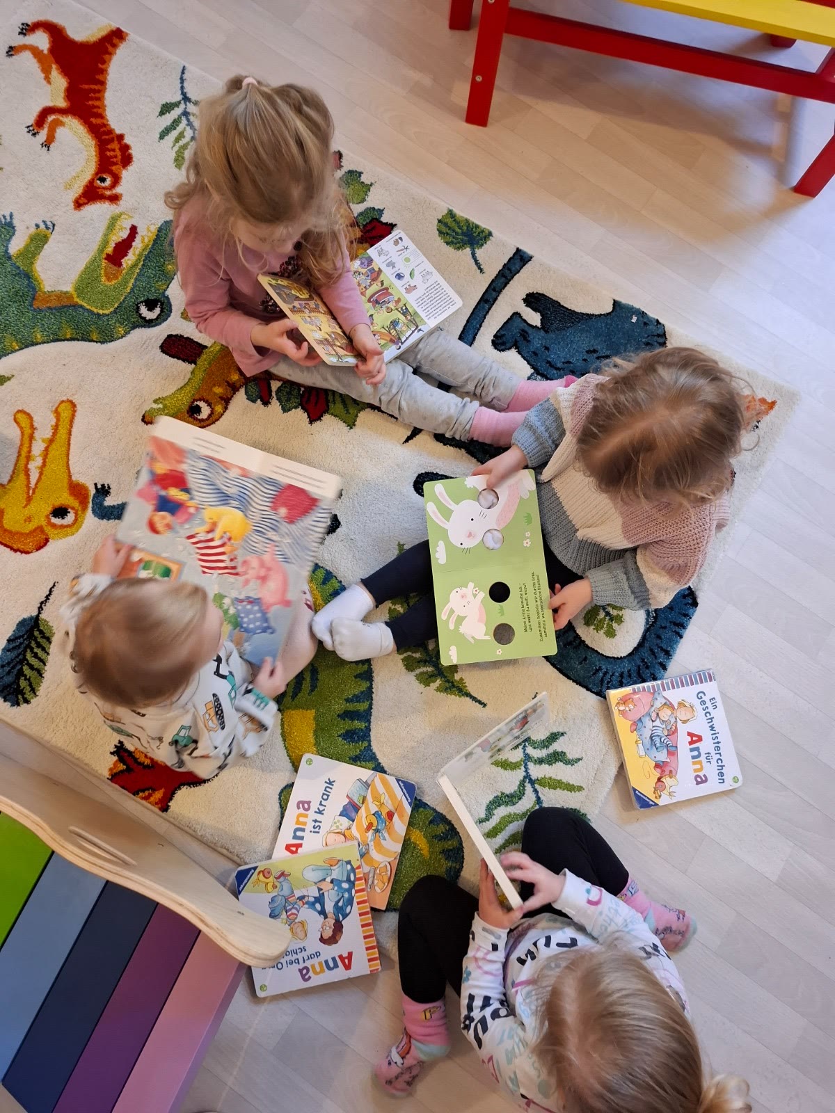 Kinder schauen gemeinsam Bilderbücher auf dem Spielteppich an